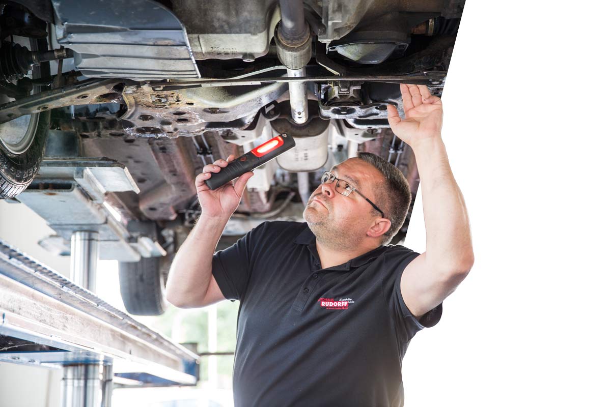 Bild von einem Mitarbeiter, der ein Fahrzeug von unten untersucht